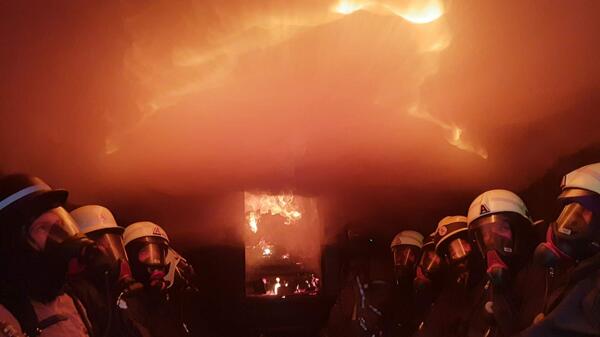 Bild vergr&ouml;&szlig;ern: Feuerwehrm�nner und Feuerwehrfrau im Flashover Container  Hei�ausbildung M�hlleithen 2018