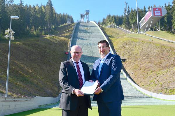 Bild vergr&ouml;&szlig;ern: Staatsekret�r G�nther Schneider (l.) �berreicht den F�rdermittelbescheid an den Vorsitzenden des Zweckverbandes Vogtland Arena und B�rgermeister von Klingenthal Thomas Hennig.