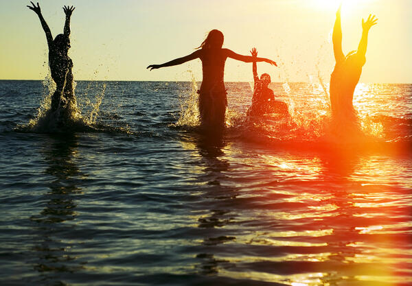 Bild vergr&ouml;&szlig;ern: Das Bild zeigt junge Menschen beim Sonnenuntergang im Wasser.