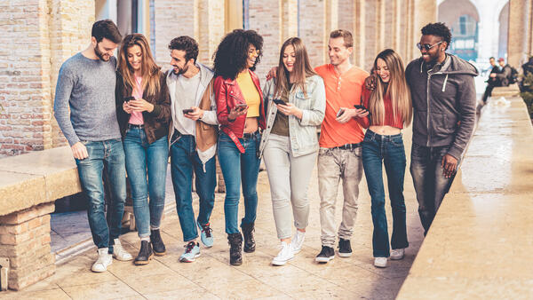Bild vergr&ouml;&szlig;ern: Das Bild zeigt eine Gruppe fr�hlicher junger Menschen die sich im Stadtzentrum treffen. Sie haben Spa� mit ihren Smartphones und sozialen Medien, gehen zusammen spazieren und plaudern zusammen.