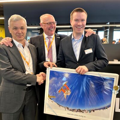Bild vergr&ouml;&szlig;ern: Landrat Rolf Keil gratuliert Paul Wehner, dem Leiter der neuen Jugendherberge und Dr. G&uuml;nther Schneider, dem Pr&auml;sidenten des Deutschen Jugendherbergswerks zur Er&ouml;ffnung. Er &uuml;bergibt dabei ein gerahmtes Poster mit einem springenden Snowboarder.