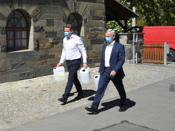 Bild vergr&ouml;&szlig;ern: Landrat Rolf Keil und Dr. Marc Kusche, der Gesch&auml;ftsf&uuml;hrer der Wernesgr&uuml;ner Brauerei GmbH, tragen je einen gespendeten Kanister mit Handdesinfektionsmittel, zur &Uuml;bergabe an die SBW Vogtlandkreis gGmbH