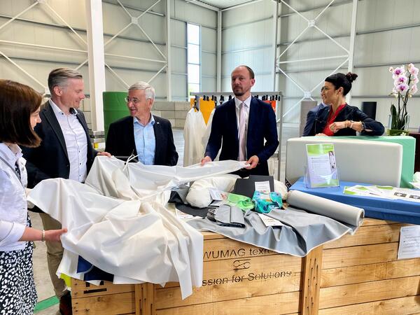 Bild vergr&ouml;&szlig;ern: Die vogtl&auml;ndische Bundestagsabgeordnete Yvonne Magwas, Axel Seidel, Gesch&auml;ftsf&uuml;hrer der Friedrich Seidel GmbH aus Schreiersgr&uuml;n, Landrat Rolf Keil, Marco Wanderwitz, der Ostbeauftragte der Bundesregierung und Mareen G&ouml;tz, Gesch&auml;ftsf&uuml;hrerin der VOWALON Beschichtung GmbH zeigen einen Schutzkittel. Das Mehrwegprodukt wird in der Region produziert.