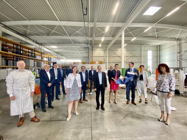 Bild vergr&ouml;&szlig;ern: Vertreter der regionalen Textilwirtschaft und der Politik stehen zusammen und pr&auml;sentieren in der Region produzierte Artikel, wie einen Mehrwegkittel und speziell beschichteten Stoff.