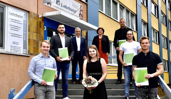 Bild vergr&ouml;&szlig;ern: Unsere Auszubildenden stehen gemeinsam mit Landrat Rolf Keil und Ausbildungsleiterin Heike D&ouml;lling auf einer Treppe und halten ihre Zeugnisse sowie einen Blumenstrau&szlig; in H&auml;nden.
