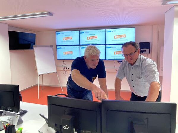 Bild vergr&ouml;&szlig;ern: Mitarbeiter Peter Gebhardt und der Leiter des Sachgebiets Brand- und Katastrophenschutz Ingo Gla� stehen im Lagezentrum Katastrophenschutz im Landratsamt Vogtlandkreis vor sechs gro�en Monitoren.