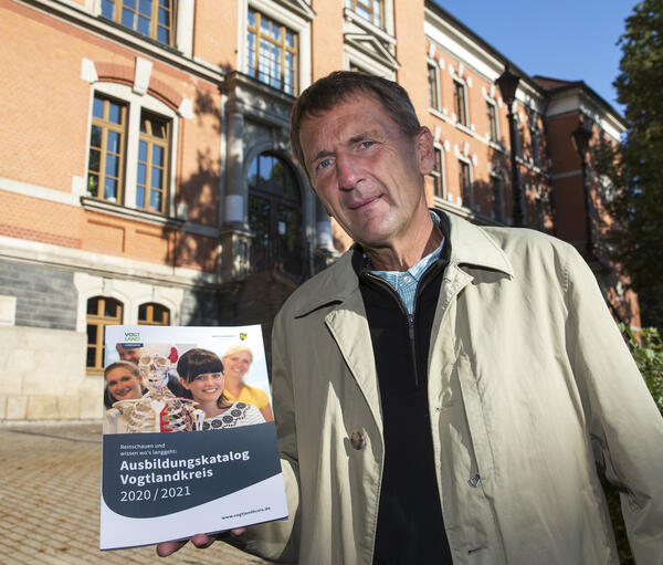Bild vergr&ouml;&szlig;ern: Hartmut Briese h&auml;lt den Ausbildungskatalog Vogtlandkreis in die Kamera. Dabei steht er vor dem Gymnasium in Oelsnitz.