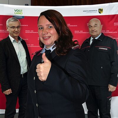 Bild vergr&ouml;&szlig;ern: Das Bild zeigt Landrat, Rolf Keil, links und rechts der Vorsitzende des Kreisfeuerwehrverbandes Andreas Schubert. In ihrer Mitte steht Feuerwehrfrau Sandra Neubert. Als eines der Gesichter der Marketingkampagne ertrat die junge Kameradin stellvertretend ihre 3.625 aktiven &raquo;Kollegen&laquo; der vogtl&auml;ndischen Wehren. 
Der abschlie&szlig;ende Wunsch der Ehrenamtlichen konnte auch nicht anders lauten: &raquo;Retten. L&ouml;schen. Bergen. Sch&uuml;tzen - Sei(d) mit dabei!&laquo;