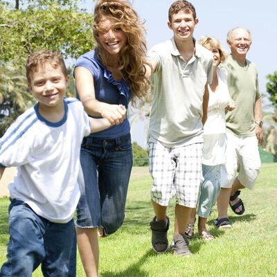 Bild vergr&ouml;&szlig;ern: Eine Familie von jung bis alt h&auml;lt sich an den H&auml;nden und l&auml;uft lachend &uuml;ber die Wiese