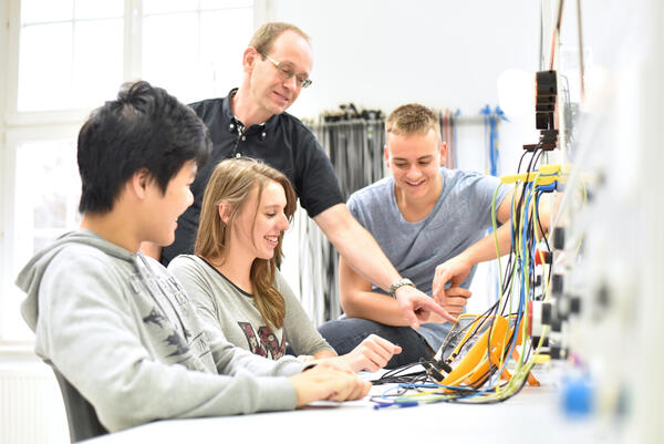 Bild vergr&ouml;&szlig;ern: Auf dem Bild sieht man einen Lehrer, der drei Sch�lern Elektrotechnik erkl�rt.