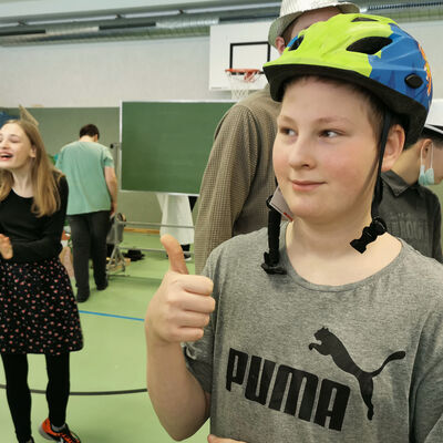 Bild vergr&ouml;&szlig;ern: Ein Junge tr&auml;gt einen blau-gr&uuml;nen Fahrradhelm und hebt den Daumen.