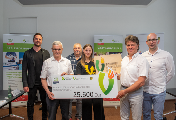Bild vergr&ouml;&szlig;ern: Das Bild zeigt Jan Rodewald vom Sachbereich Sport des Landratsamtes, Landrat Rolf Keil, Organisationsleiter der Vogtlandspiele Ralf Schmutzler, Botschafter Gina Spranger, Pr&auml;sident des Kreissportbundes Vogtland Steffen Fugmann und Kreissportbund-Gesch&auml;ftsf&uuml;hrer Michael Degenkolb. Bei der Pressekonferenz wurde ein symbolischer Scheck in H&ouml;he von 25.600 Euro &uuml;bergeben.