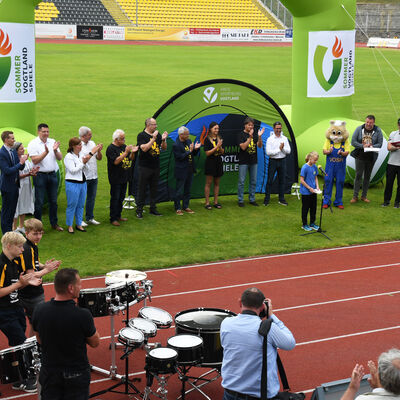 Das Bild zeigt Vertreter der Politik bei der Er&ouml;ffnungsfeier der Vogtlandspiele. Eine junge Sportlerin steht am Mikrofon und h&auml;lt den olymischen Eid ab. Alle stehen auf dem gr&uuml;nen Rasen im Vogtlandstadion.