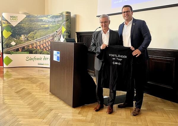 Bild vergr&ouml;&szlig;ern: Auf dem Bild sieht man den Gesch&auml;ftsf&uuml;hrer des Tourismusverbandes Vogtland, Dr. Andreas Kraus. Er &uuml;berreicht als Dankesch&ouml;n f&uuml;r die jahrelange, gute Zusammenarbeit ein T-Shirt an den scheidenden Landrat Rolf Keil.