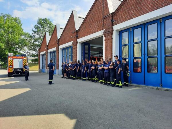 Bild vergr&ouml;&szlig;ern: Das Bild zeigt mehrere Kameraden vogtl&auml;ndischer Feuerwehren vor den Toren einer Feuerwehrger&auml;tehalle. Im Hintergrund ist ein L&ouml;schfahrzeug der Feuerwehr zu sehen.