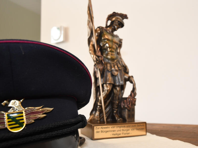Bild vergr&ouml;&szlig;ern: Eine Floriansfigur neben einem traditionellen Feuerwehrhut