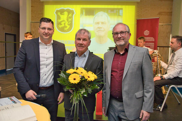 Bild vergr&ouml;&szlig;ern: Das Bild zeigt Landrat Thomas Hennig, Volkhardt Kramer, der als "Auerbachs B&uuml;rgerpreistr&auml;ger 2022" ausgezeichnet wurde und den Auerbacher Oberb&uuml;rgermeister Jens Scharff. Volkhardt Kramer h&auml;lt einen Blumenstrau&szlig; mit gelben Blumen.