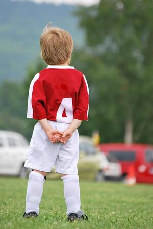 Bild vergr&ouml;&szlig;ern: Das Bild zeigt die R&uuml;ckenansicht eines Kindes mit einem roten Fu&szlig;balldress, wei&szlig;en Fu&szlig;ballshorts und wei&szlig;en Kniestr&uuml;mpfen.