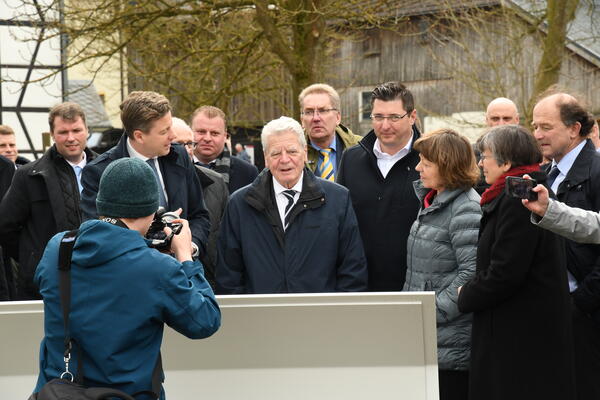 Bild vergr&ouml;&szlig;ern: Das Bild zeigt Joachim Gauck und seine Frau Daniela Schadt inmitten einer gro&szlig;en Gruppe von Menschen. Alle stehen vor einer Informationstafel, die an der Gedenkst&auml;tte in M&ouml;dlareuth zu finden sind.