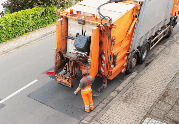 Bild vergr&ouml;&szlig;ern: Abfallbeh�lter wird an einem orangefarbenen M�llfahrzeug gekippt.