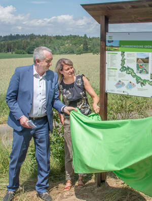 Bild vergr&ouml;&szlig;ern: Auf dem Bild sieht man die Enth&uuml;llung der Info-Tafel im Rahmen der &Uuml;bergabe des vollendeten Flurbereinigungsverfahrens "Gr&uuml;nes Band I" nahe Loddenreuth. Links: Staatsminister Regionalentwicklung Thomas Schmidt, daneben Katrin Weller (Landratsamt Vogtlandkreis).