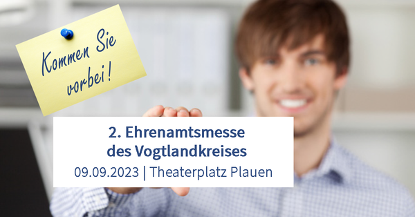 Bild vergr&ouml;&szlig;ern: Das Bild zeigt einen jungen Mann, der ein Schild in die Kamera h&auml;lt. Auf diesem stehen die Daten zur 2. Ehrenamtsmesse des Vogtlandkreises. Diese findet am 9. September 2023 auf dem Theaterplatz in Plauen statt.