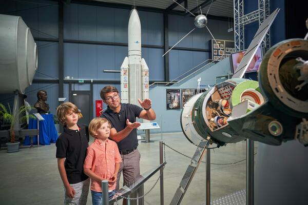 Bild vergr&ouml;&szlig;ern: Das Bild zeigt Raumfahrtausstellung in Morgenr&ouml;the Rautenkranz. Im Vordergrund ist ein Vater zu sehen, der seinen beiden S&ouml;hnen etwas zur Ausstellung erkl&auml;rt.