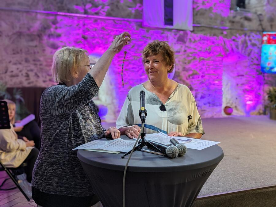 Zwei &auml;ltere Damen stehen an einem Tisch. Die eine h&auml;lt eine bunte Perlenkette in der Hand.
