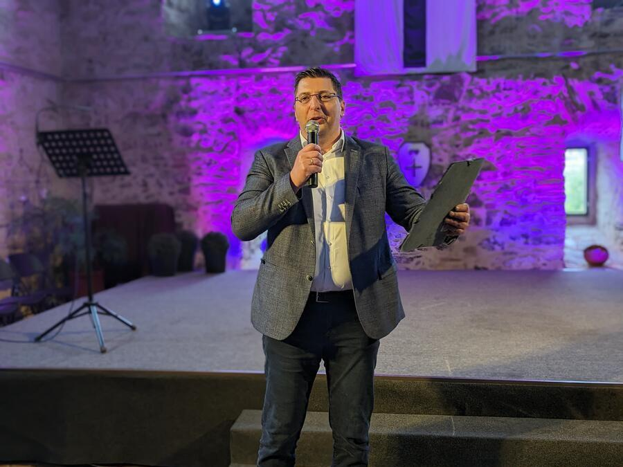 Landrat Thomas Hennig h&auml;lt eine Rede. In einer Hand hat er ein Mikrofon, in der anderen eine Mappe.
