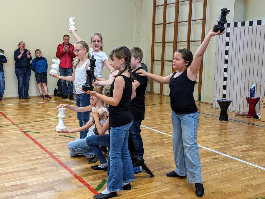 Eine Gruppe Kinder h&auml;lt gro&szlig;e Schachfiguren in den H&auml;nden.