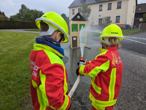 Bild vergr&ouml;&szlig;ern: Zwei Kinder halten einen Schlauch auf ein Holzhaus.