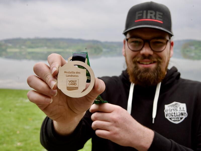 Ein Mann h&auml;lt eine Medaille aus Holz in die Kamera.
