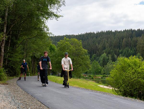 Bild vergr&ouml;&szlig;ern: Das Bild zeigt mehrere Jugendliche, die mit Rollern, Skateboards und Inlinern den neuen asphaltierten Weg an der Talsperre ausprobieren.