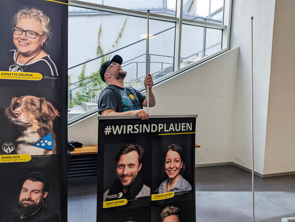 Bild vergr&ouml;&szlig;ern: Fotograf Kenny Pool baut ein Roll-Up auf. Er steckt ein Banner auf einen Stab.