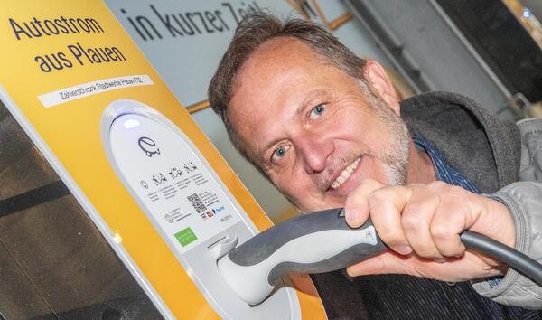Bild vergr&ouml;&szlig;ern: Das Bild zeigt den Energiebauftragten des Vogtlandkreises, Uwe Hergert. Er h�lt mit einer Hand die Pistole einer E-Lades�ule, an der Elektroautos geladen werden k�nnen.