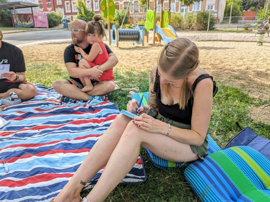 Eine junge Frau sitzt auf einer Decke und schreibt auf einen Zettel.