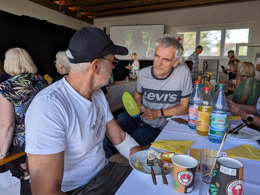 Ein &auml;lterer Herr wird interviewt. Ein Reporter h&auml;lt ihm ein Mikrofon vor sein Gesicht.