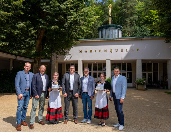 Bild vergr&ouml;&szlig;ern: Vor der Marienquelle in Bad Elster mit Heilwasser: Thomas R&ouml;h (Tourismus- und Gewerbeverein), Florian Merz (Generalmusikdirektor), Landrat Thomas Hennig, B&uuml;rgermeister Olaf Schlott und Jens B&ouml;hmer (S&auml;chsische Staatsb&auml;der GmbH) mit zwei Brunnenm&auml;dchen
