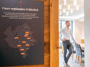Bild vergr&ouml;&szlig;ern: Das Bild zeigt eine Karte mit den Orten, aus denen die regionalen Produkte zum regionalen Fr&uuml;hst&uuml;ck im Tannenhaus stammen. Im Hintergrund steht Gesch&auml;ftsf&uuml;hrer Tobias Werner.