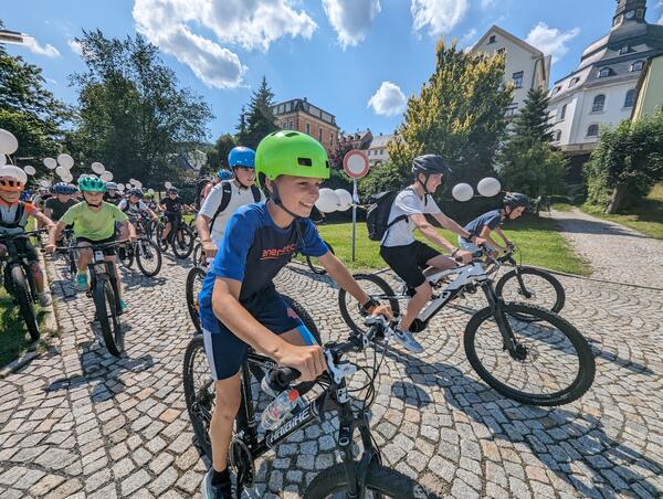 Bild vergr&ouml;&szlig;ern: Radfahrer fahren gemeinsam. Sie haben wei�e Luftballons an ihren K�rper befestigt.