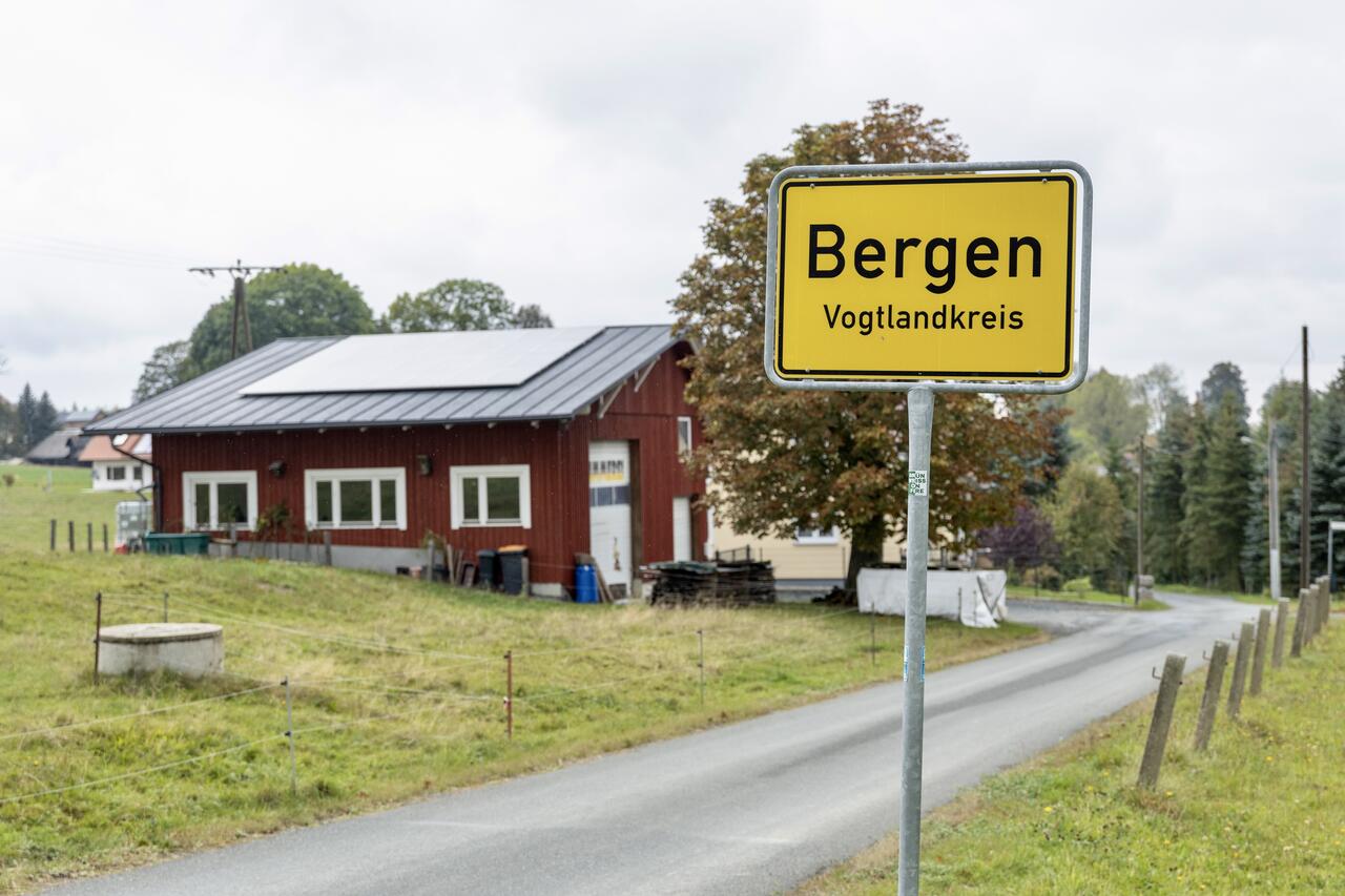 Bild vergr&ouml;&szlig;ern: Ortseingangsschild der Gemeinde Bergen, im Hintergrund ein dunkelrotes Geb�ude.