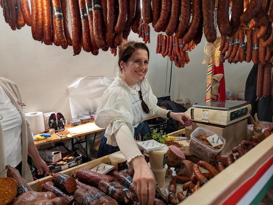 An einer Fleischtheke verkauft eine junge Frau Wurstwaren.