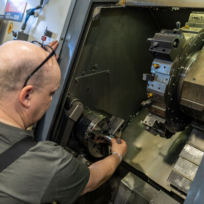 Bild vergr&ouml;&szlig;ern: Ein Mitarbeiter best&uuml;ckt die Drehmaschine mit einem Werkst&uuml;ck.