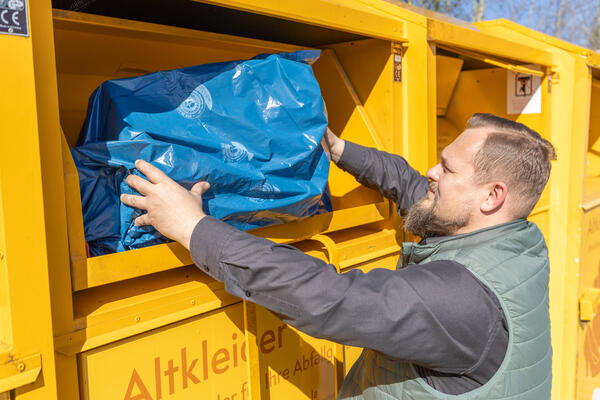 Bild vergr&ouml;&szlig;ern: Ein Mann steckt einen Sack Altkleider in einen Container