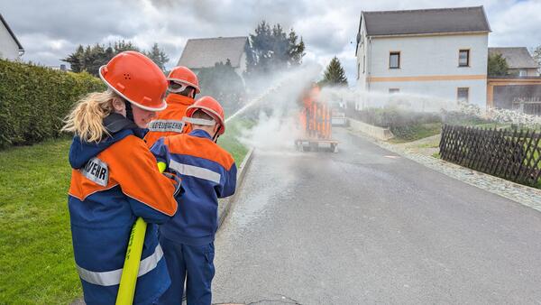 Bild vergr&ouml;&szlig;ern: Drei Kameraden der Jugendfeuerwehr halten mit einem Wasserstrahl auf das brennende Haus.