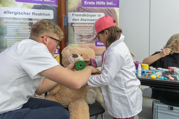 Bild vergr&ouml;&szlig;ern: Ein M�dchen verbindet den Arm eines Teddyb�rs.