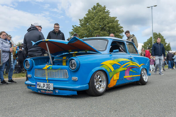 Bild vergr&ouml;&szlig;ern: Ein auff&auml;llig getunter blauer Trabant steht auf dem Festivalgel&auml;nde, umringt von interessierten Besucherinnen und Besuchern.