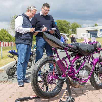 Bild vergr&ouml;&szlig;ern: Landrat Thomas Hennig und Sternquell-Gesch&auml;ftsf&uuml;hrer Jan Gerbeth begutachten ein violettes Simson-Moped und machen Notizen auf Klemmbrettern.