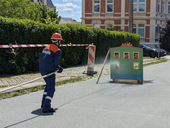 Ein Mitglied der Jugendfeuerwehr l&ouml;scht ein Brandhaus aus Holz.