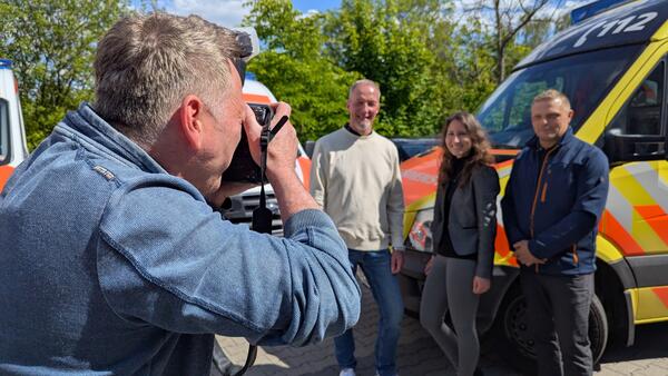 Bild vergr&ouml;&szlig;ern: Drei Gr�nder werden vor einem Rettungswagen fotografiert.